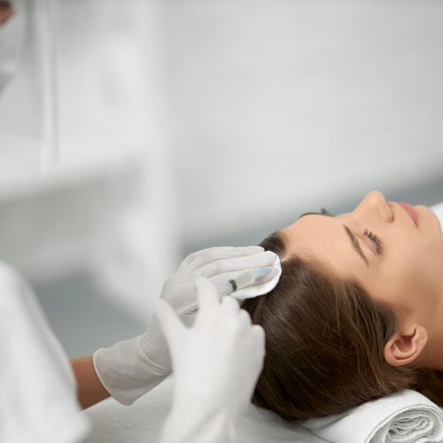 Side view of young cute brunette woman on procedure for improvements hair condition. Concept of different procedure for hair restoration in professional beauty salon.
